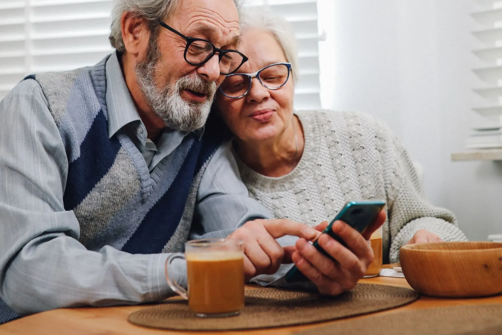 Una pareja mayor consulta información en un teléfono, sentada a la mesa de su casa